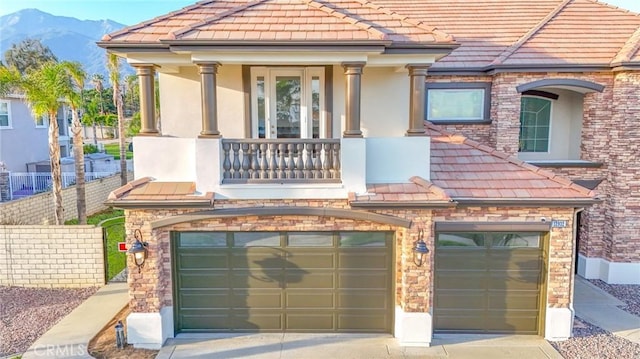 view of front facade with driveway, a balcony, an attached garage, fence, and stucco siding