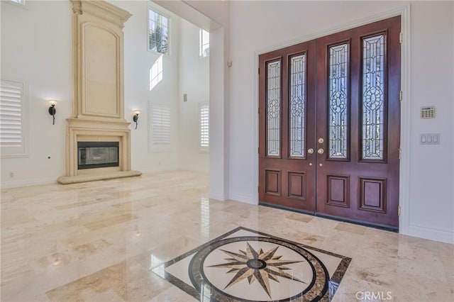 foyer with a glass covered fireplace, marble finish floor, a towering ceiling, and baseboards