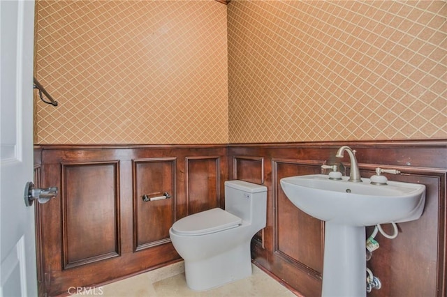 half bath with a wainscoted wall, a decorative wall, toilet, and wallpapered walls