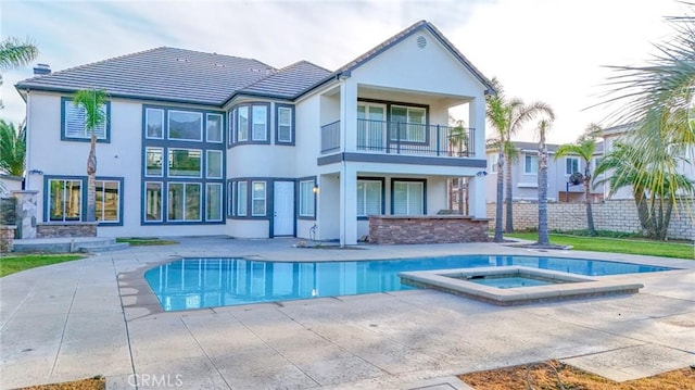 rear view of property with a patio, stucco siding, a pool with connected hot tub, fence, and a balcony