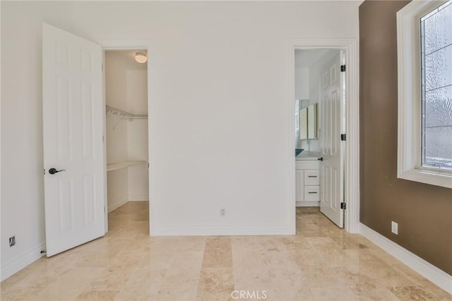 unfurnished bedroom featuring baseboards, a walk in closet, and connected bathroom