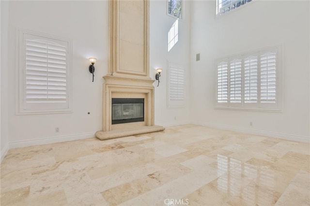 unfurnished living room with a large fireplace, a high ceiling, and baseboards