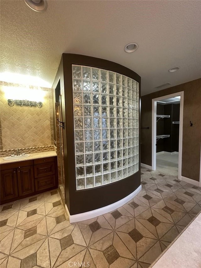 interior space featuring recessed lighting, decorative backsplash, a sink, a textured ceiling, and baseboards