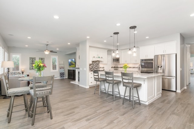 kitchen featuring tasteful backsplash, white cabinets, an island with sink, appliances with stainless steel finishes, and light wood-style floors