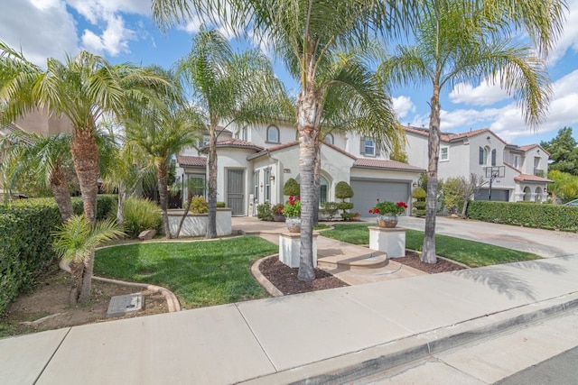 mediterranean / spanish-style house with a garage, driveway, a tiled roof, stucco siding, and a front yard