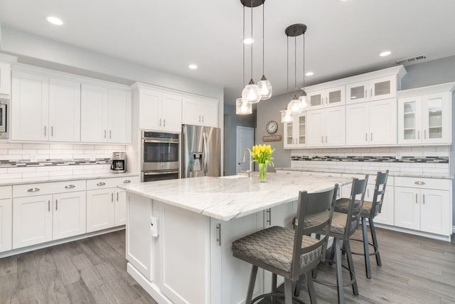 kitchen featuring a center island with sink, visible vents, appliances with stainless steel finishes, white cabinets, and a kitchen bar