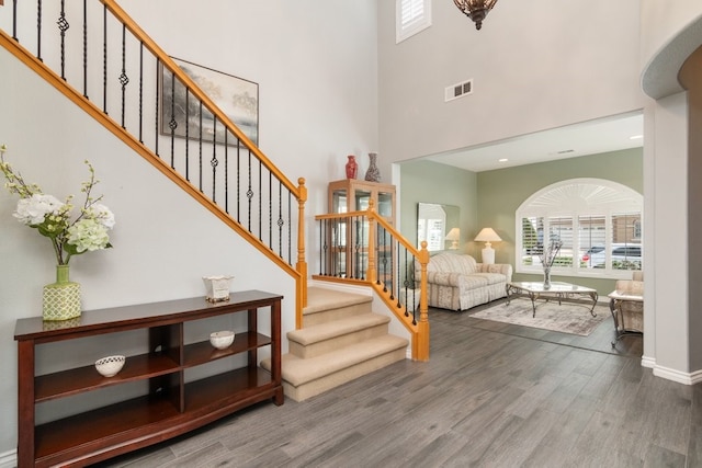 foyer entrance featuring baseboards, visible vents, wood finished floors, a high ceiling, and stairs