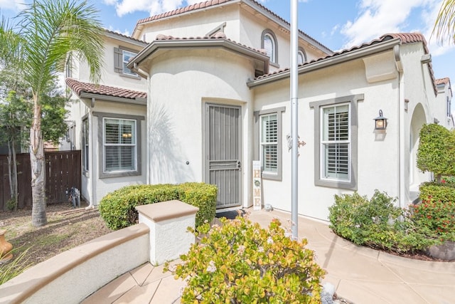 property entrance featuring stucco siding, fence, and a tiled roof