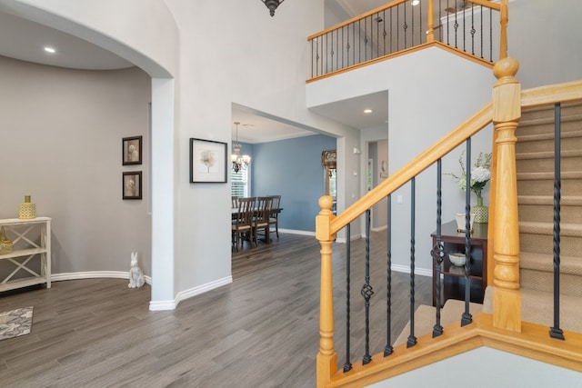 staircase featuring arched walkways, a chandelier, wood finished floors, a towering ceiling, and baseboards