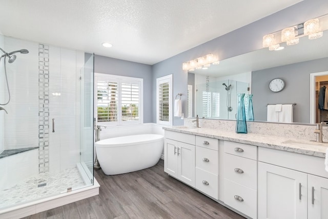 bathroom featuring double vanity, a stall shower, a sink, and wood finished floors