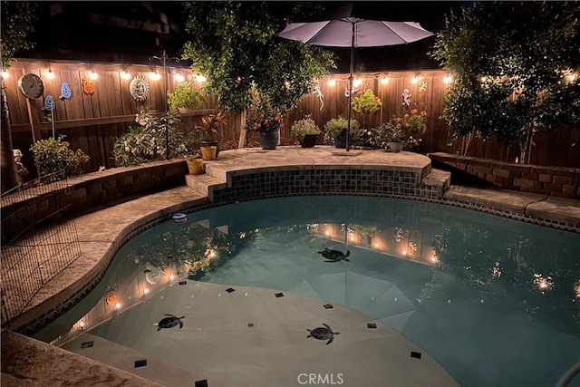 pool at twilight with a fenced backyard and a jacuzzi