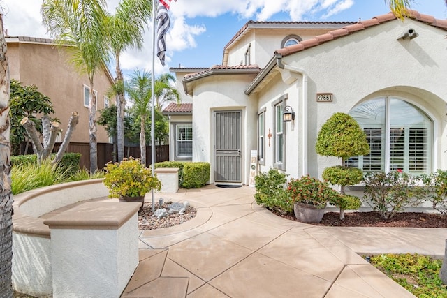 view of exterior entry with a tile roof, fence, and stucco siding