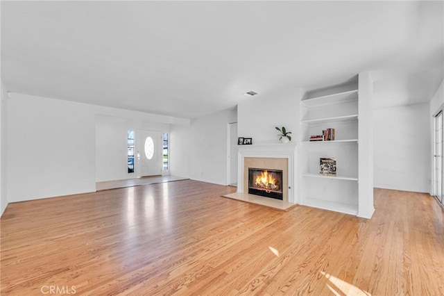 unfurnished living room featuring light wood-type flooring, visible vents, built in features, and a glass covered fireplace