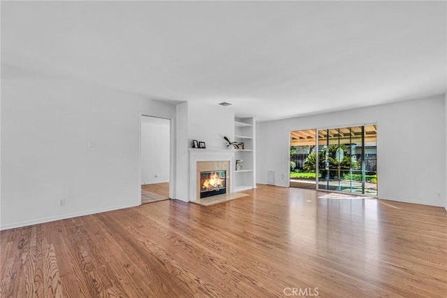 unfurnished living room featuring built in shelves, a tile fireplace, baseboards, and wood finished floors