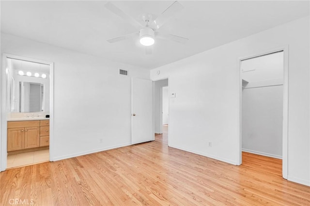 unfurnished bedroom with a walk in closet, a closet, visible vents, light wood-style flooring, and ensuite bathroom