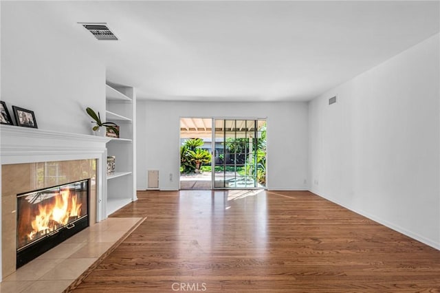 unfurnished living room featuring built in shelves, visible vents, a tiled fireplace, and wood finished floors