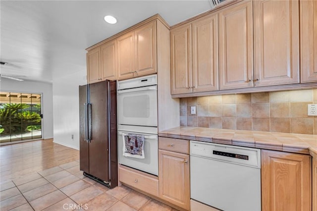 kitchen with tile counters, white appliances, backsplash, and light brown cabinetry