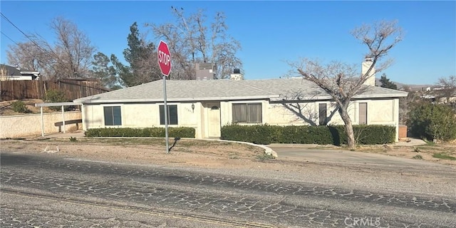 ranch-style home with a shingled roof, stucco siding, a chimney, and fence