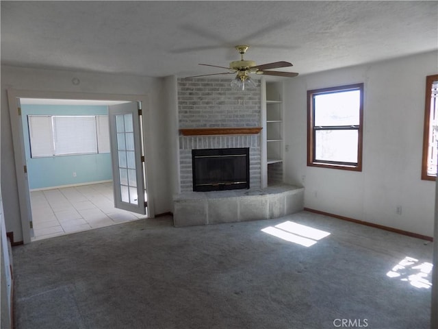 unfurnished living room featuring a brick fireplace, built in shelves, ceiling fan, carpet flooring, and a textured ceiling