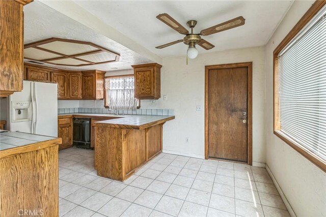 11671 Jacaranda Ave, Hesperia, CA 92345 - kitchen with brown cabinets, dishwasher, white fridge with ice dispenser, tile countertops, and a peninsula