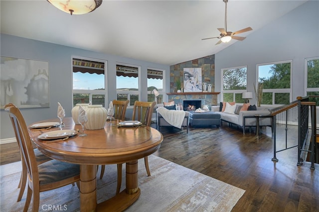 dining space featuring high vaulted ceiling, ceiling fan, a stone fireplace, and wood finished floors