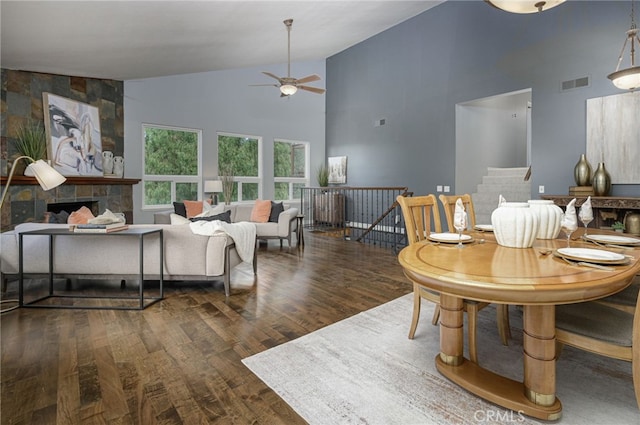 living area with visible vents, a ceiling fan, wood finished floors, a fireplace, and high vaulted ceiling