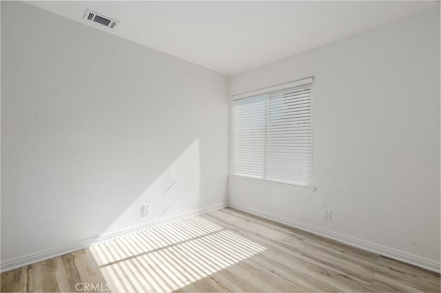 spare room with light wood-type flooring, visible vents, and baseboards