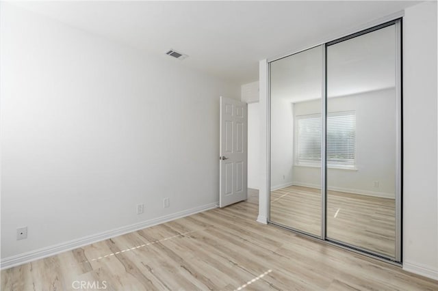 unfurnished bedroom with light wood-style floors, a closet, visible vents, and baseboards