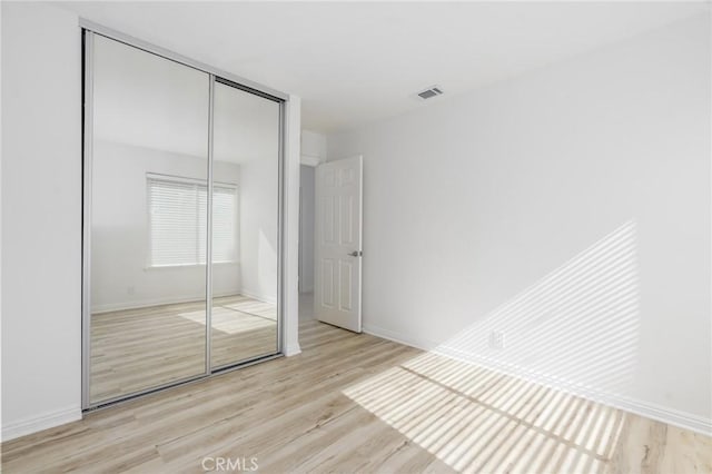 unfurnished bedroom featuring a closet, visible vents, baseboards, and wood finished floors