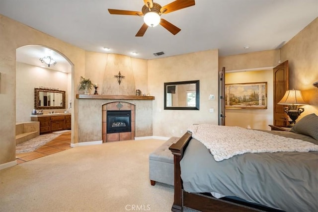 carpeted bedroom with a tile fireplace, baseboards, visible vents, and ensuite bath