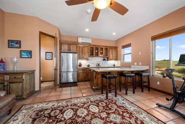 kitchen featuring brown cabinetry, glass insert cabinets, freestanding refrigerator, a peninsula, and backsplash