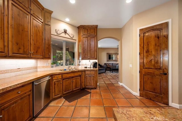 kitchen with arched walkways, decorative backsplash, brown cabinetry, a sink, and dishwasher