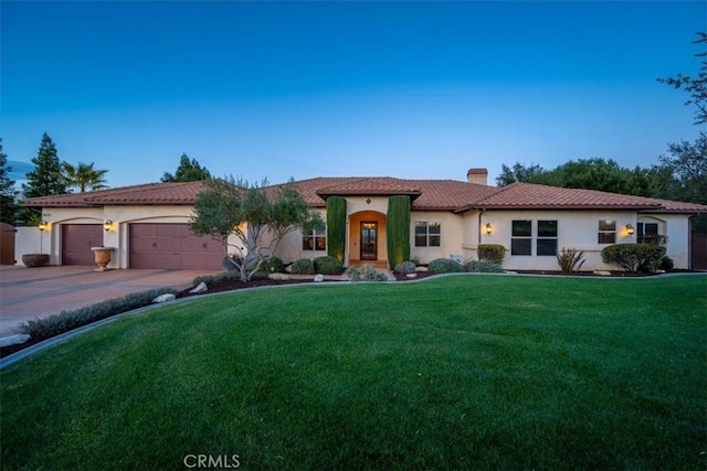 mediterranean / spanish home with a tile roof, concrete driveway, stucco siding, a front lawn, and a chimney