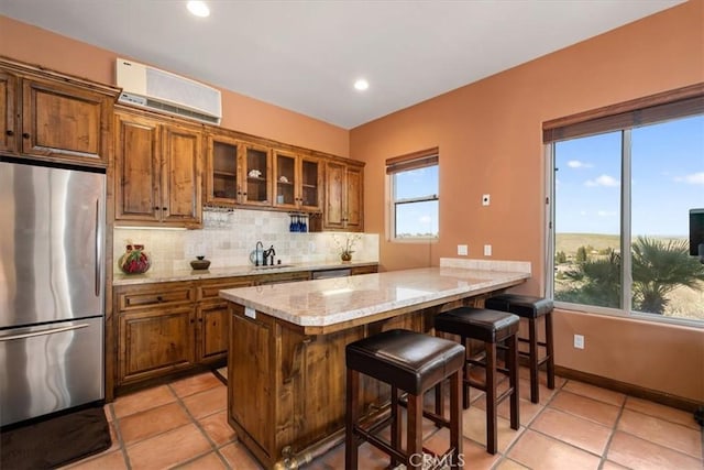 kitchen featuring a wall unit AC, brown cabinetry, decorative backsplash, and freestanding refrigerator