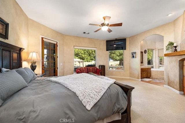 carpeted bedroom with arched walkways, ensuite bathroom, a ceiling fan, visible vents, and baseboards