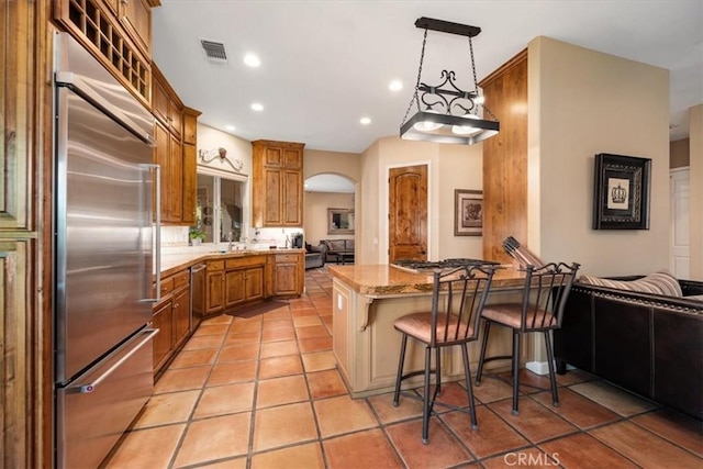 kitchen with arched walkways, stainless steel appliances, visible vents, brown cabinetry, and a kitchen breakfast bar