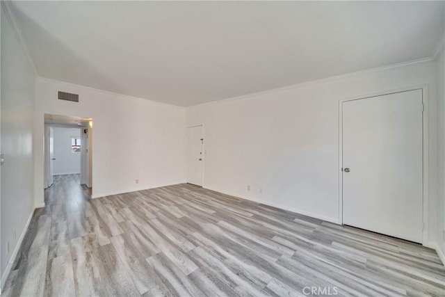 spare room with ornamental molding, light wood-style flooring, visible vents, and baseboards