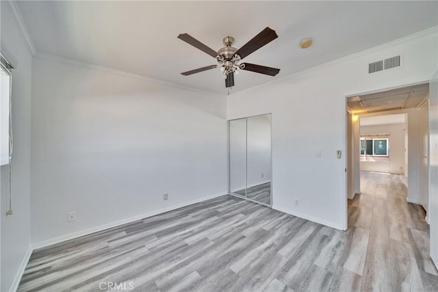 unfurnished bedroom featuring a closet, visible vents, light wood-style floors, attic access, and ornamental molding