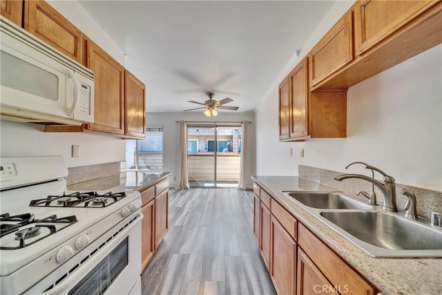 kitchen featuring light wood-type flooring, white appliances, brown cabinetry, and a sink