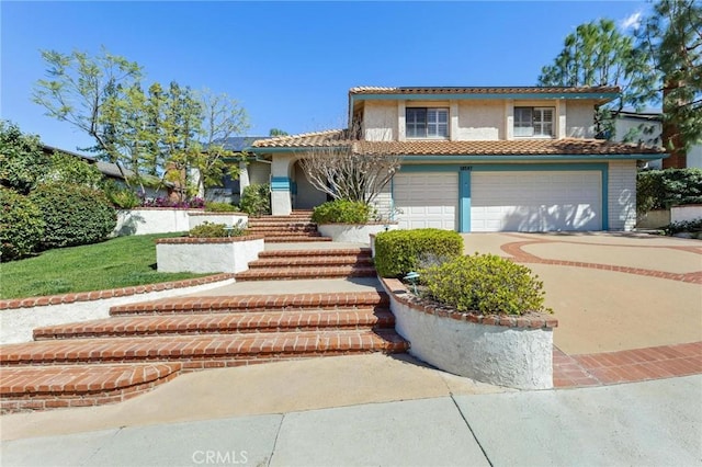 mediterranean / spanish home with concrete driveway, a tiled roof, an attached garage, and stucco siding