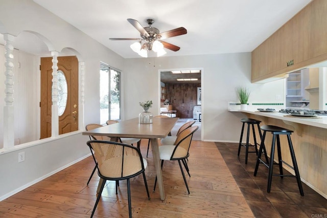 dining space with a ceiling fan, arched walkways, dark wood finished floors, and baseboards