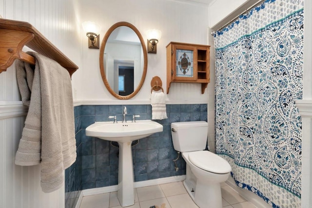 full bath featuring a shower with shower curtain, toilet, a wainscoted wall, tile patterned floors, and tile walls