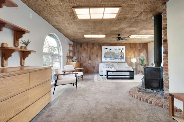 living area featuring a wood stove, light carpet, ceiling fan, and wooden walls