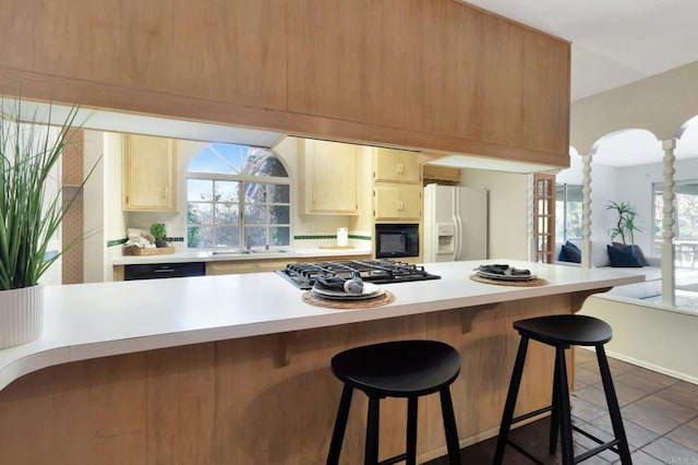 kitchen featuring decorative columns, white refrigerator with ice dispenser, a kitchen breakfast bar, light countertops, and gas stovetop