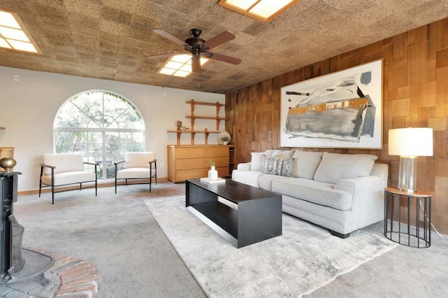 living area with carpet floors, wood walls, a wood stove, baseboards, and ceiling fan