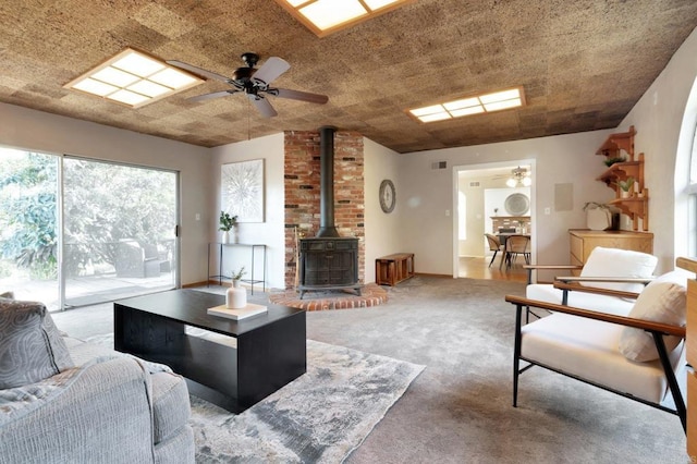 carpeted living room featuring ceiling fan, visible vents, and a wood stove