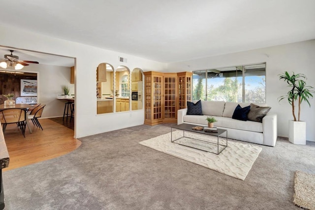 living room featuring carpet floors, a ceiling fan, arched walkways, and visible vents