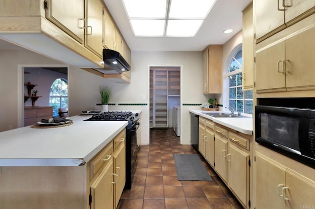 kitchen with a sink, light countertops, plenty of natural light, washing machine and dryer, and black appliances