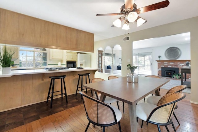 dining area with dark wood-style flooring, a fireplace, arched walkways, a ceiling fan, and visible vents