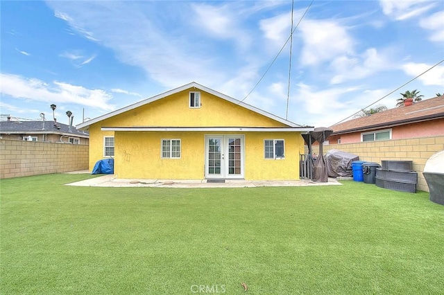 rear view of house with french doors, a fenced backyard, a lawn, and stucco siding